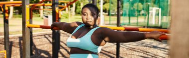Spor giyim sektöründe Afro-Amerikalı bir kadın oyun parkının önünde duruyor, vücudunun pozitifliğini ve gücünü gösteriyor..