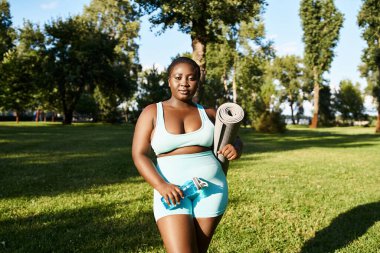 Spor kıyafetli bir Afrikalı Amerikalı kadın açık havada spor minderi tutuyor, vücut pozitifliği ve gücü somutlaştırıyor..