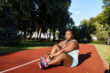 Spor giyimli Afrikalı bir Amerikalı kadın tenis kortunda oturuyor, dışarıda egzersiz yapmaya ara veriyor..