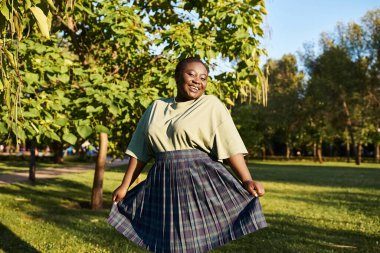 A plus-size African-American woman stands gracefully in the summer grass, wearing a flowing skirt and exuding body positivity. clipart