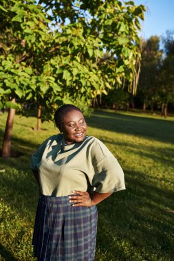 A plus-size African American woman, standing confidently in the grass, with her hands on her hips in a body-positive stance. clipart