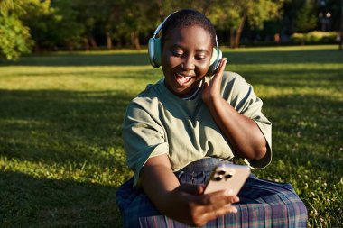 A carefree young boy relaxes on the grass, listening intently to his music, lost in the melodies. clipart