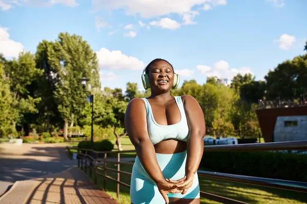 An African American woman with crossed arms stands confidently on a bench, embracing her strength and body positivity.