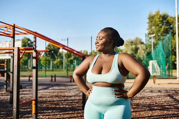 Spor giyimli Afrikalı bir Amerikalı kadın oyun parkının önünde güvenle duruyor, açık havada egzersiz yapıyor..