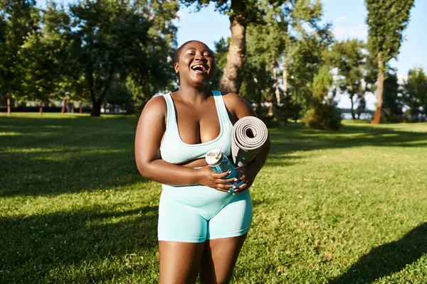 スポーツマットを保持しながら体のポジティブさを示す青いボディスーツのアフリカ系アメリカ人女性 — ストック写真
