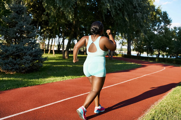 An African American woman in sportswear runs along a red track, showcasing body positivity and athleticism.