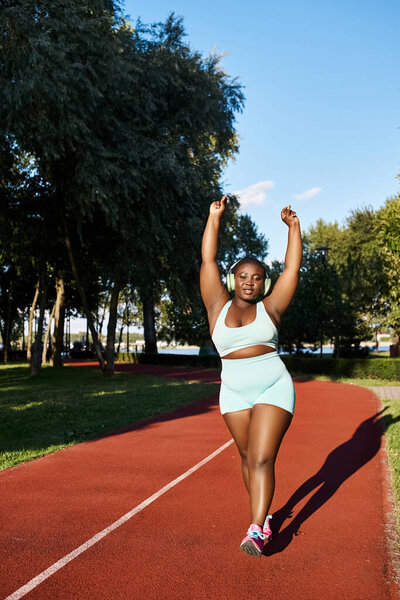 An African American woman in sportswear runs on a track, showcasing her athleticism and body positivity.