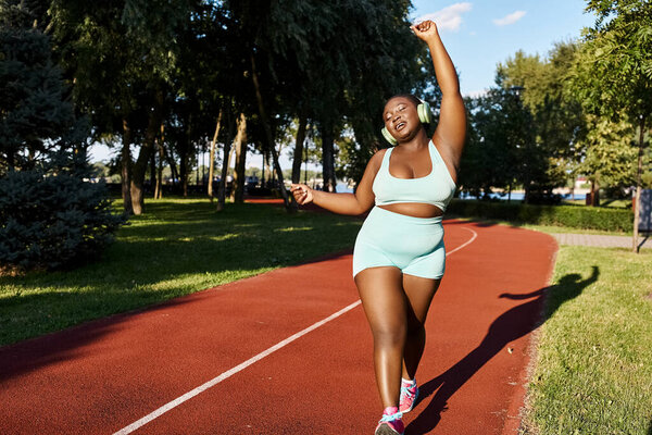 An African American woman in sportswear runs confidently along a red track outdoors, embodying body positivity and strength.