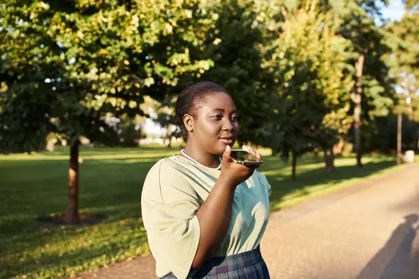 プラスサイズのアフリカ系アメリカ人女性が道端に立って 夏の暑さで電話でチャットし 体のポジティブさを受け入れる — ストック写真