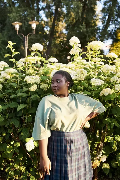 Size Afroamerykanka Stoi Pewnie Przed Krzakiem Białymi Kwiatami Obejmując Piękno — Zdjęcie stockowe