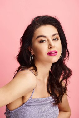 Uzun siyah saçlı, dalgalı elbiseli çarpıcı bir kadın canlı bir arkaplana karşı poz veriyor..