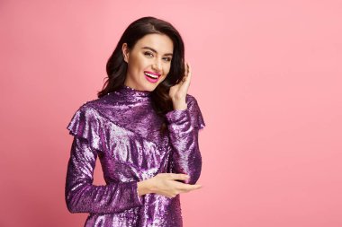 Büyüleyici bir kadın zarif bir şekilde mor bir elbiseyle canlı bir arkaplanda poz verir..