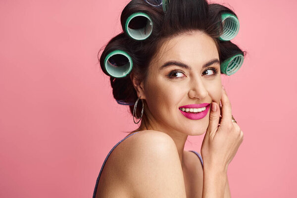 A stunning woman with curlers in her hair poses confidently against a vibrant backdrop.