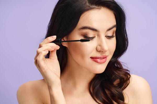 A beautiful woman with long dark hair applies mascara to her lashes.