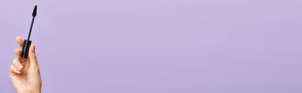 Женская рука нежно держит черную тушь на завораживающем фиолетовом фоне.