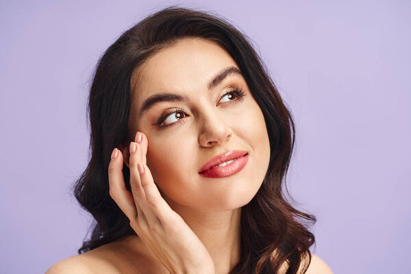 A stunning woman poses delicately with her hand gracefully resting on her face.