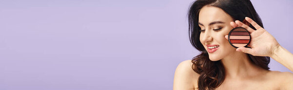 Заманчивая женщина с природной красотой держит палитру и наносит макияж.