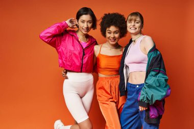 Farklı etnik kökenlere sahip üç güzel kadın bir fotoğraf için turuncu bir arkaplan önünde poz veriyor..