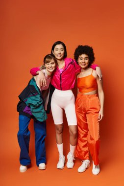 Bir grup kadın bir araya gelip turuncu bir stüdyo arkaplanına karşı güzellik ve birlik yayıyorlar..