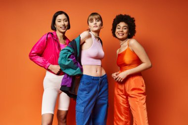 Farklı etnik kökenlere sahip üç güzel kadın canlı turuncu stüdyo arka planında çeşitliliği kutluyorlar..