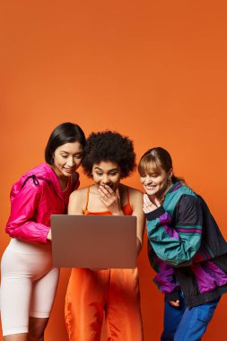 Beyaz, Asyalı ve Afro-Amerikan kökenli güzel bir grup kadın turuncu bir arka plana karşı birlikte duruyorlar..