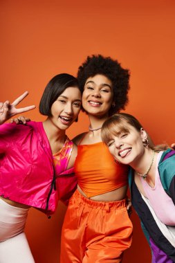 A diverse group of women stand shoulder to shoulder, showcasing beauty and strength against a vivid orange background. clipart