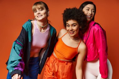 Bir grup kadın, turuncu bir stüdyonun arka planında güzelliği ve çeşitliliği sergileyerek bir arada duruyorlar..