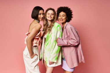 Three women of different ethnicities standing together, showcasing multicultural beauty against a pink studio backdrop. clipart