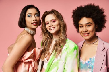 Farklı arkaplanlardan üç kadın canlı pembe bir arkaplanda yan yana durur..