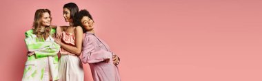 Çeşitli etnik kökenlere sahip bir grup kadın pembe bir geçmişe sahip bir stüdyoda yan yana duruyor, kardeşlik ve çeşitlilik sergiliyorlar..