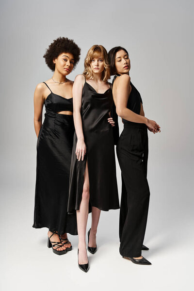 Three diverse women, Caucasian, Asian, and African American, standing elegantly in black dresses against a grey studio background.