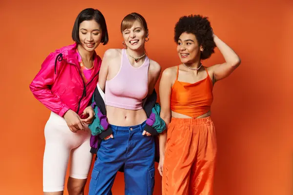 stock image Three diverse women standing side by side against an orange studio background, radiating beauty and empowerment.