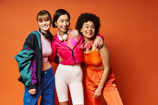 Stock image Three beautiful women representing diversity and unity, standing together against an orange background.