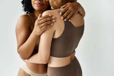 Two diverse women in cozy pastel underwear sharing a warm embrace. clipart