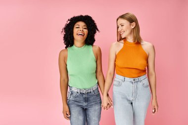 Two diverse women in stylish casual attire stand in front of a pink backdrop. clipart