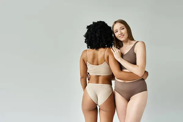 Two diverse women stand side by side in pastel underwear.