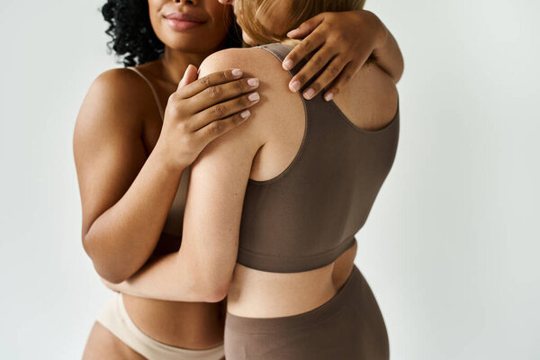 Two diverse women in cozy pastel underwear sharing a warm embrace.