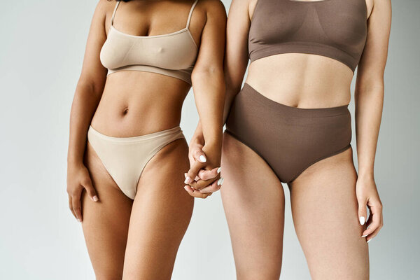 Two beautiful diverse women stand elegantly together in cozy pastel underwear.