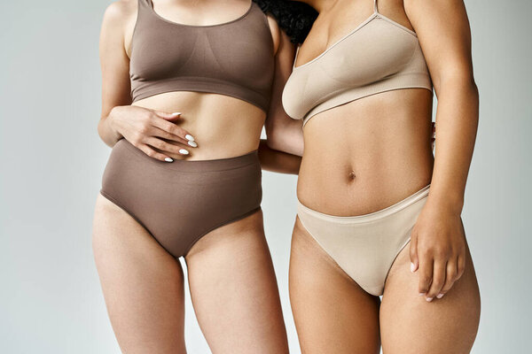 Two beautiful diverse women standing in cozy pastel underwear.
