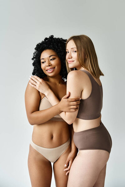 Two beautiful diverse women in cozy pastel underwear pose gracefully for a picture.