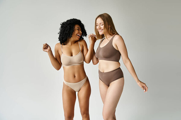 Two diverse women stand side by side in cozy pastel underwear, exuding confidence and comfort.