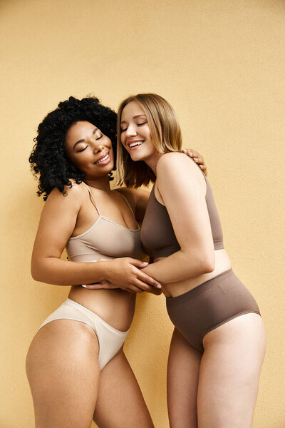 Two diverse women in cozy pastel underwear standing side by side.