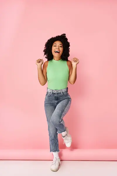 A woman in a green shirt and jeans jumps in the air.