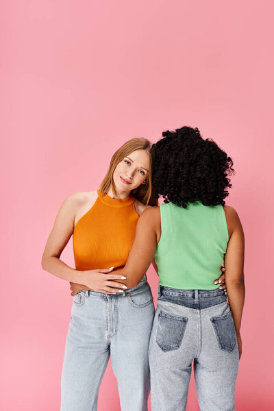 Две разные женщины в повседневной одежде стоят вместе на розовом фоне.