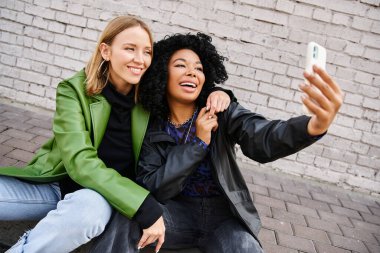 Sıradan giyinmiş iki çekici kadın cep telefonuyla selfie çekiyor..