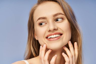 A young, blonde woman throws her head back, beaming joyfully, hands cupping her face in a studio setting. clipart