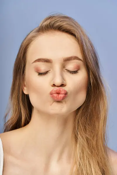 stock image A young blonde woman in a studio setting makes a funny face with her tongue out, exuding a playful and humorous vibe.