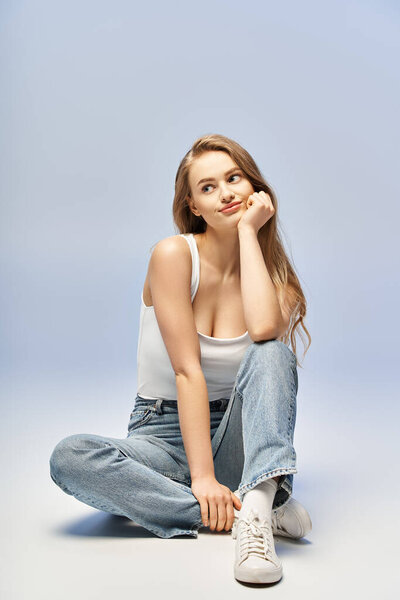 Молодая блондинка сидит на земле, ее рука лежит на голове в жесте глубокого созерцания.