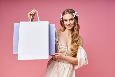 Çekici, sarı saçlı genç bir kadın stüdyo ortamında bir alışveriş çantası tutuyor..
