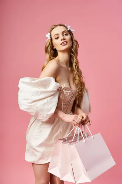 stock image Young, blonde woman in a white dress gracefully holds colorful shopping bags in a studio setting.